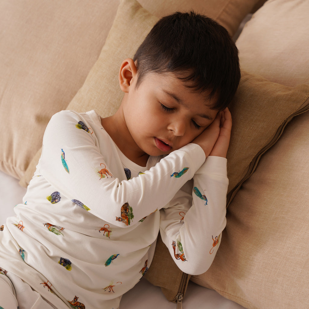 Child wearing long pajamas with animal patterns, lying on a beige couch.
