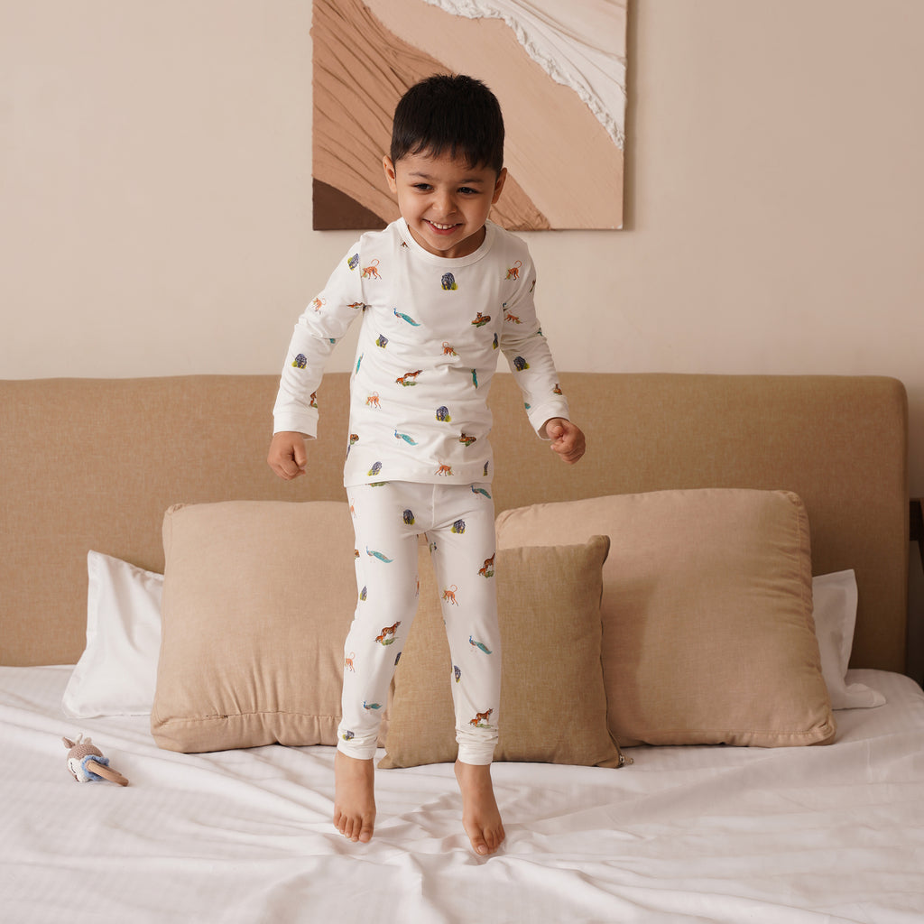 Child in long pajamas with animal print standing on a bed in a bedroom