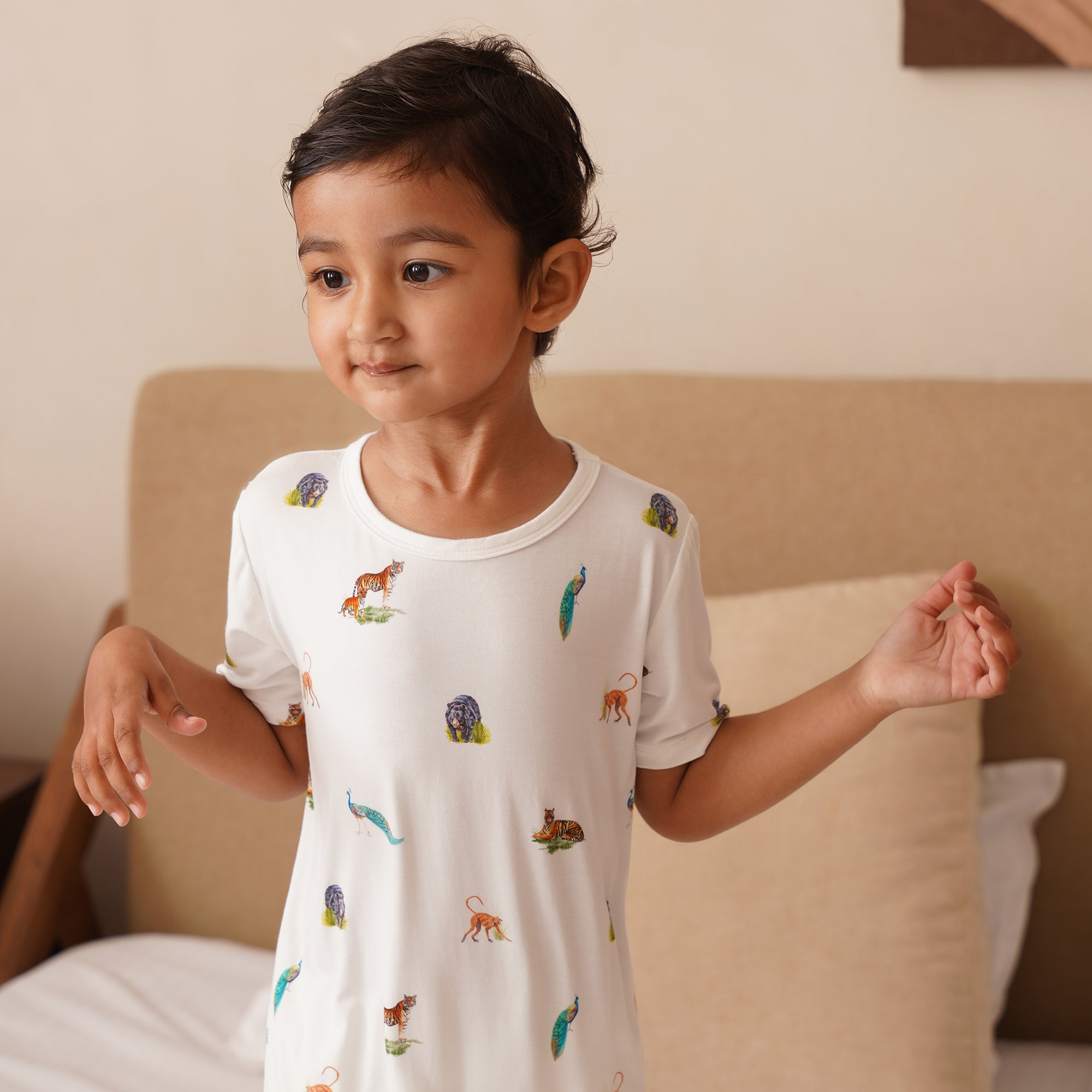 Child wearing a white nightshirt with animal prints in a bedroom setting