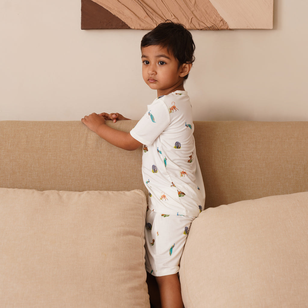 Child wearing a white short pajamas with animal prints standing on a beige couch.