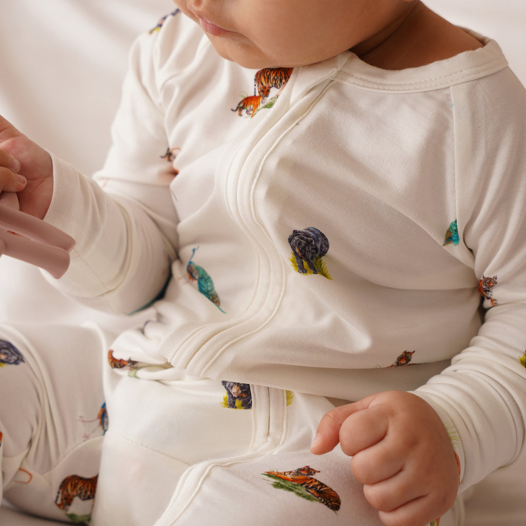 Close-up of a baby wearing a white onesie or zipsuit with animal prints on a plain background