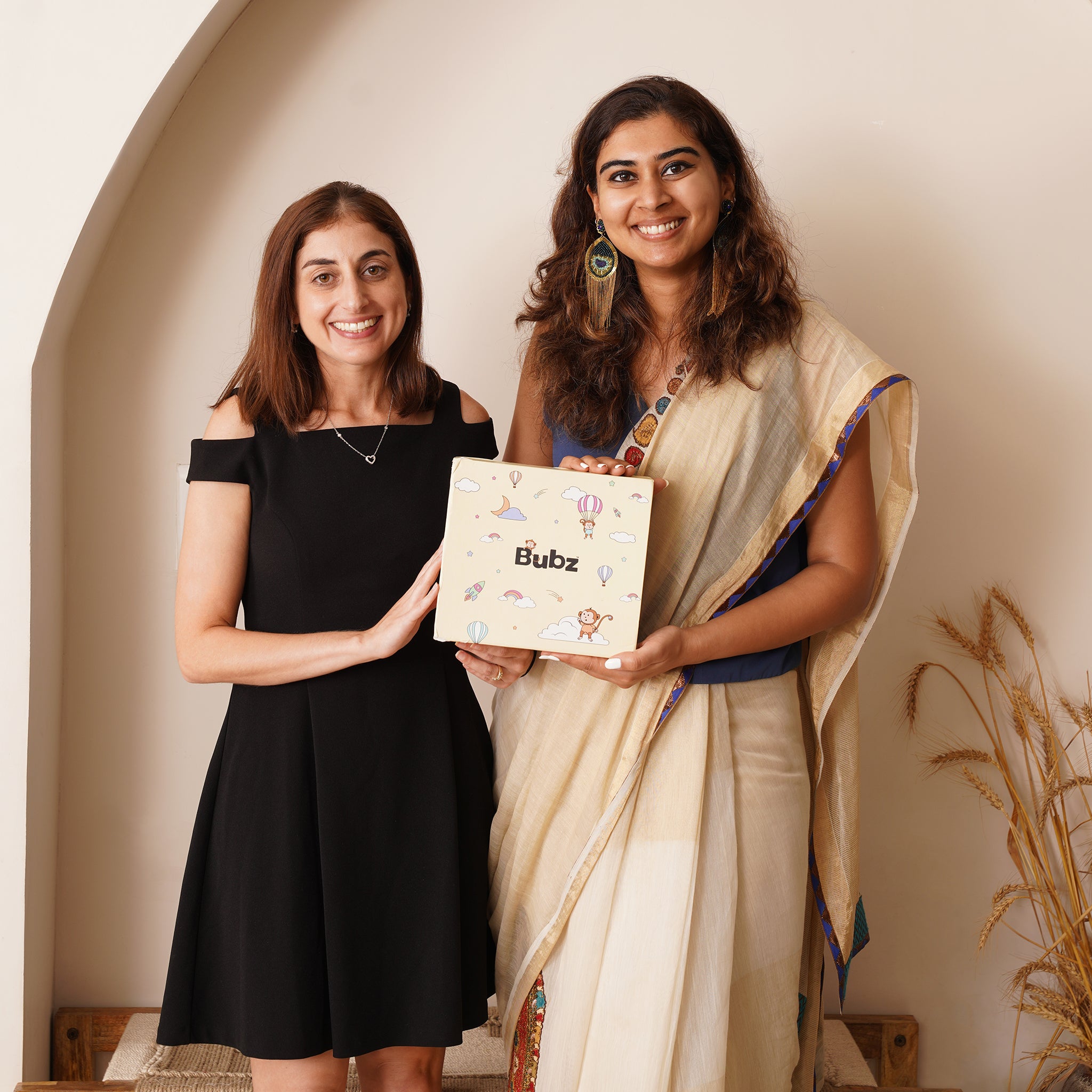 Two women holding a box labeled 'Bubz' in a warm indoor setting.