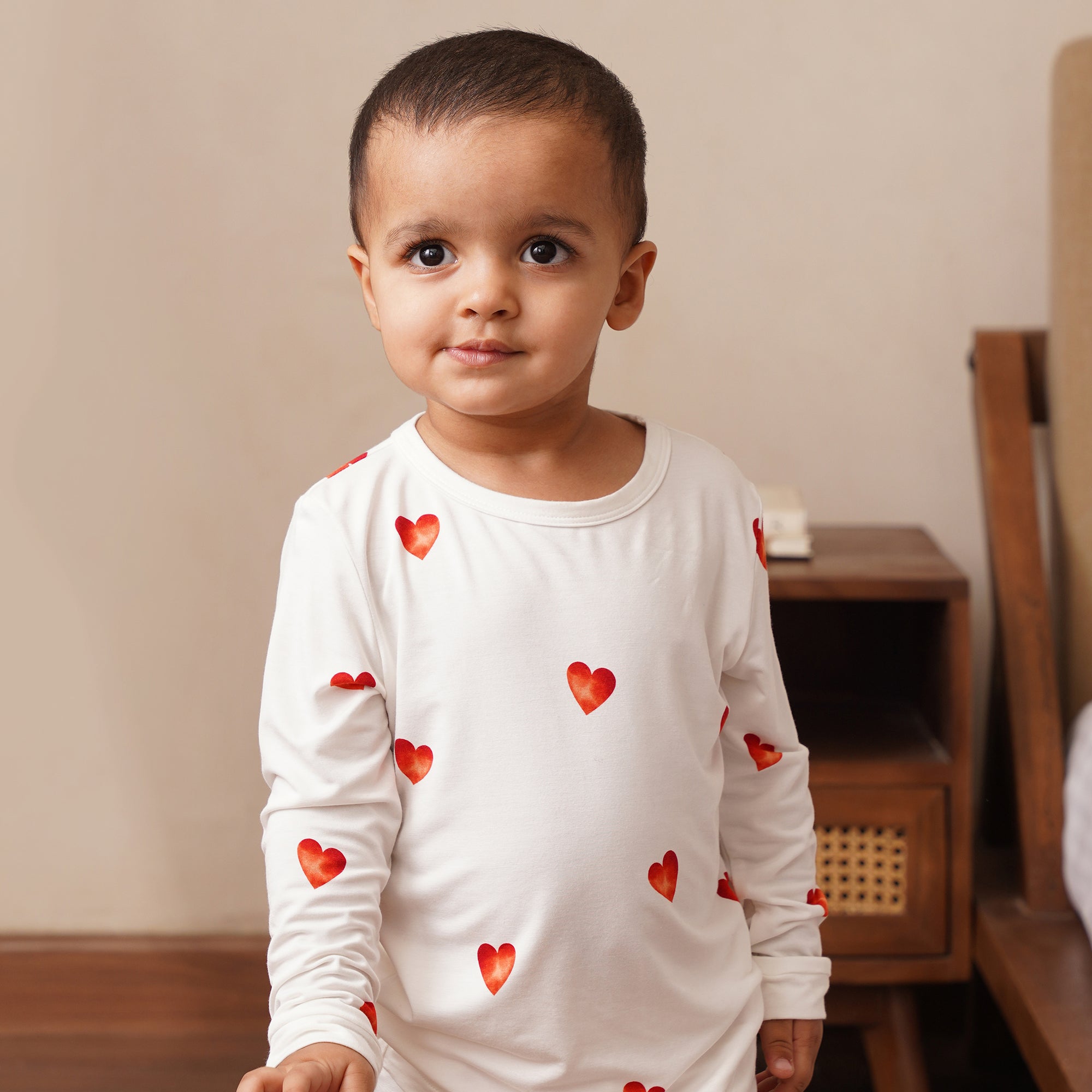 Child wearing a white long-sleeve shirt with red heart patterns in a room.