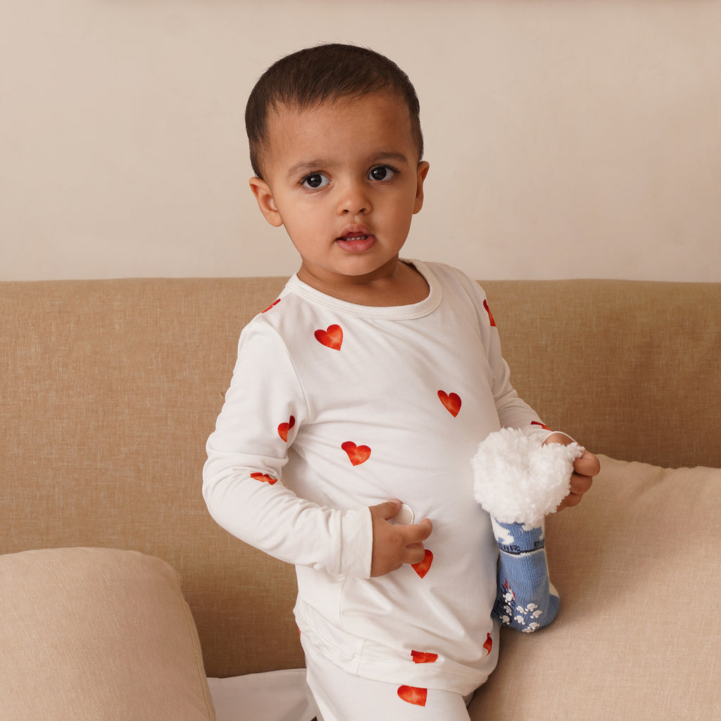 Child wearing a white long-sleeve shirt with red hearts, sitting on a beige couch.