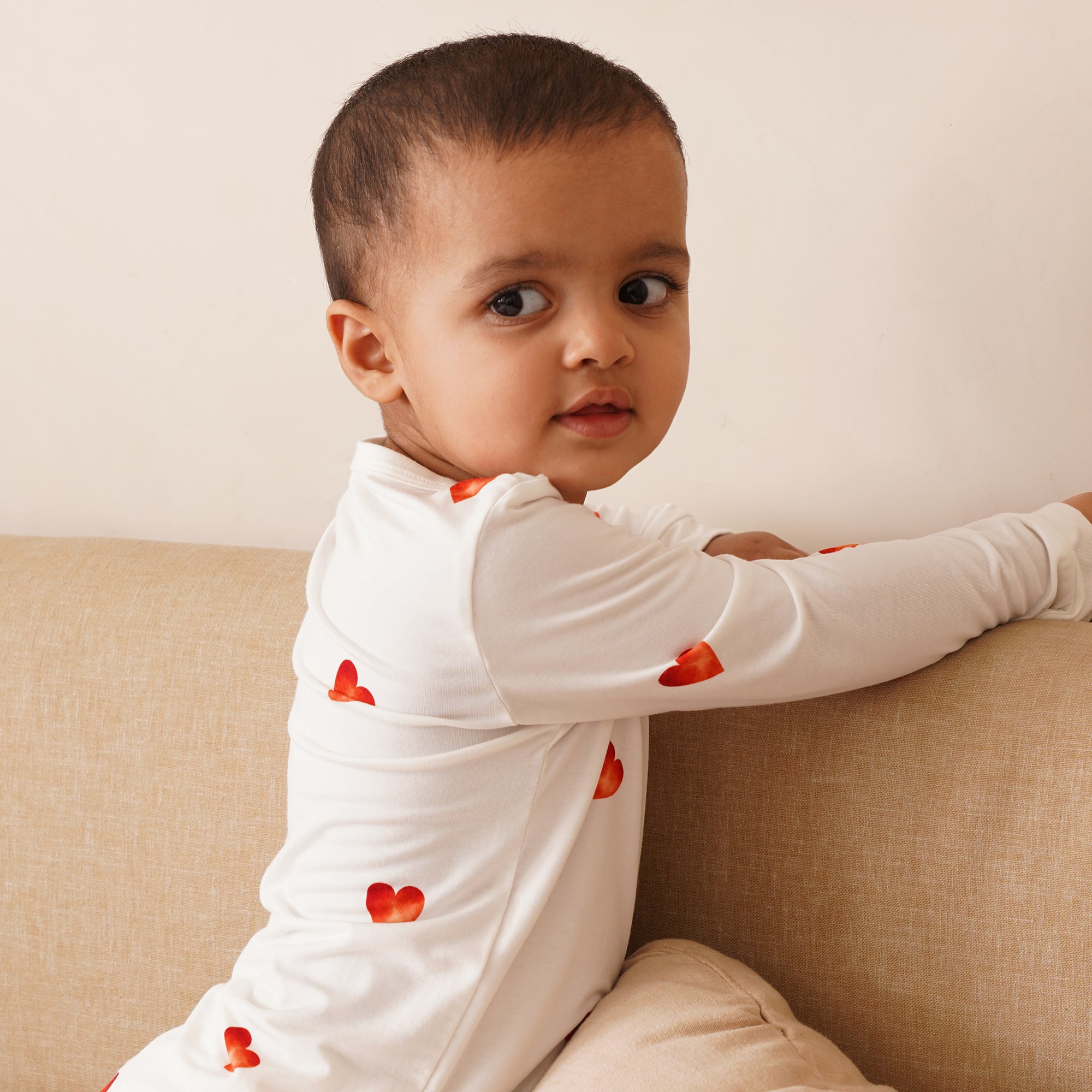 Child wearing a white long-sleeve shirt with red heart patterns, sitting on a beige couch.