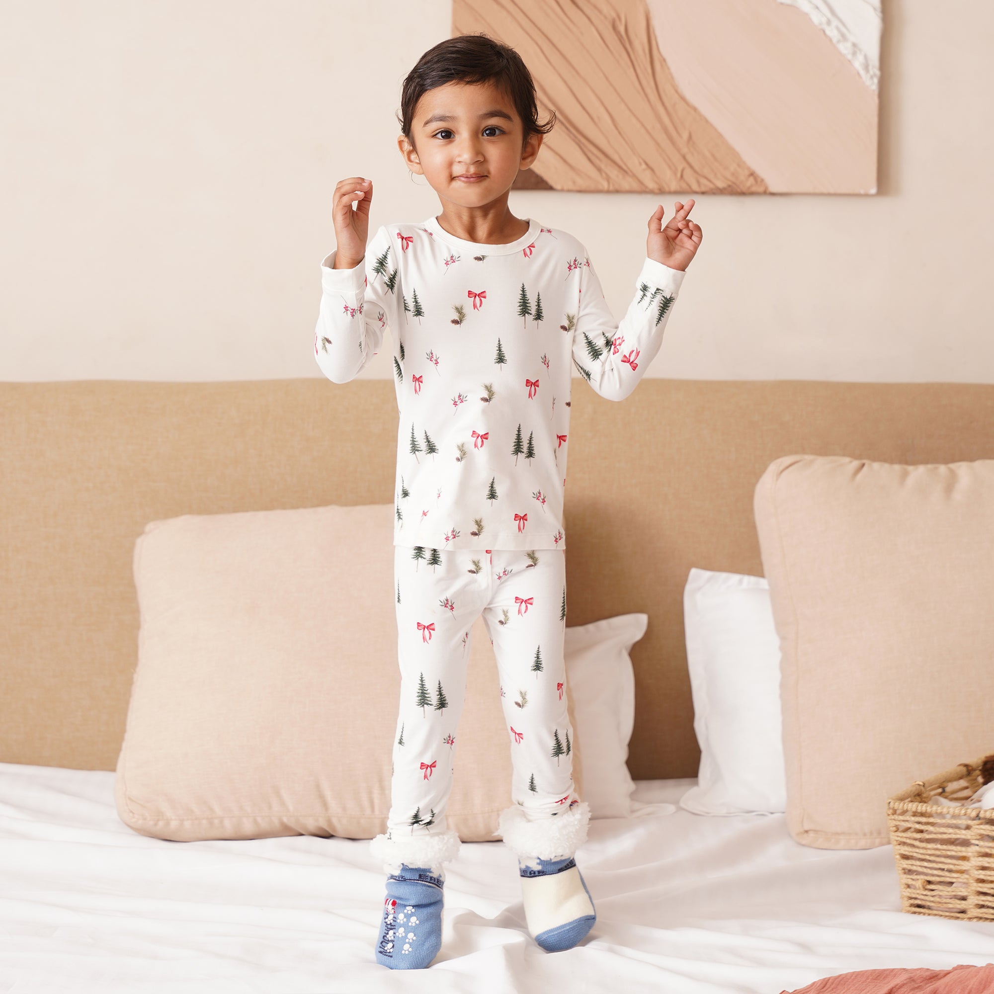 Child wearing a white pajama set with holiday prints in a bedroom setting.