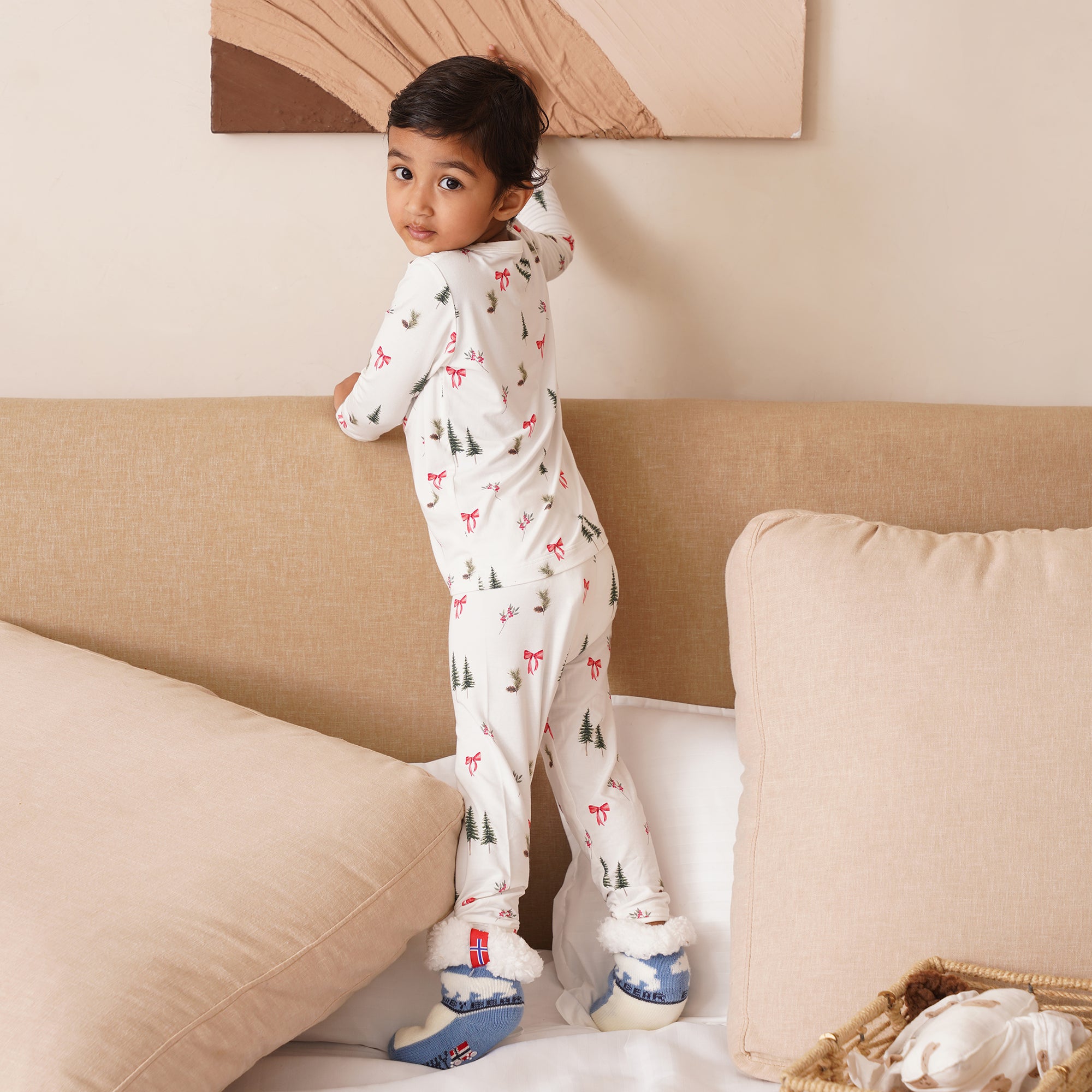 Child wearing a patterned onesie standing on a couch. Holiday themed