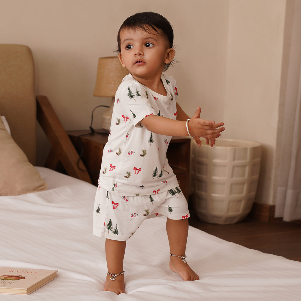Child in a white pajama set with holiday prints standing on a bed.