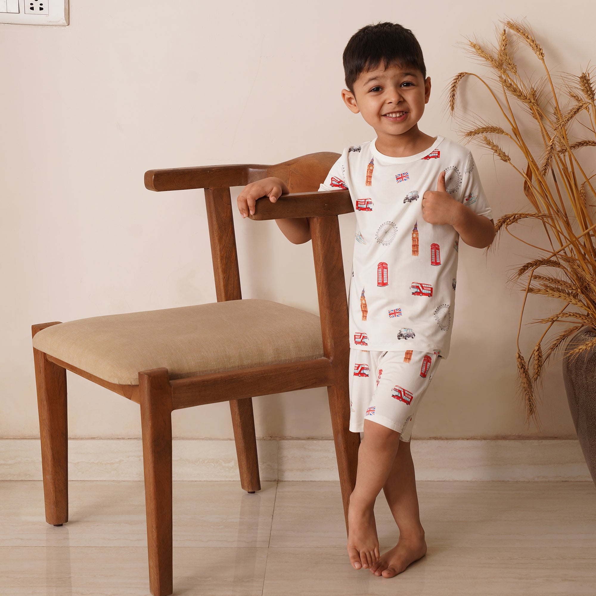 Young child in short pajamas london print standing next to a chair