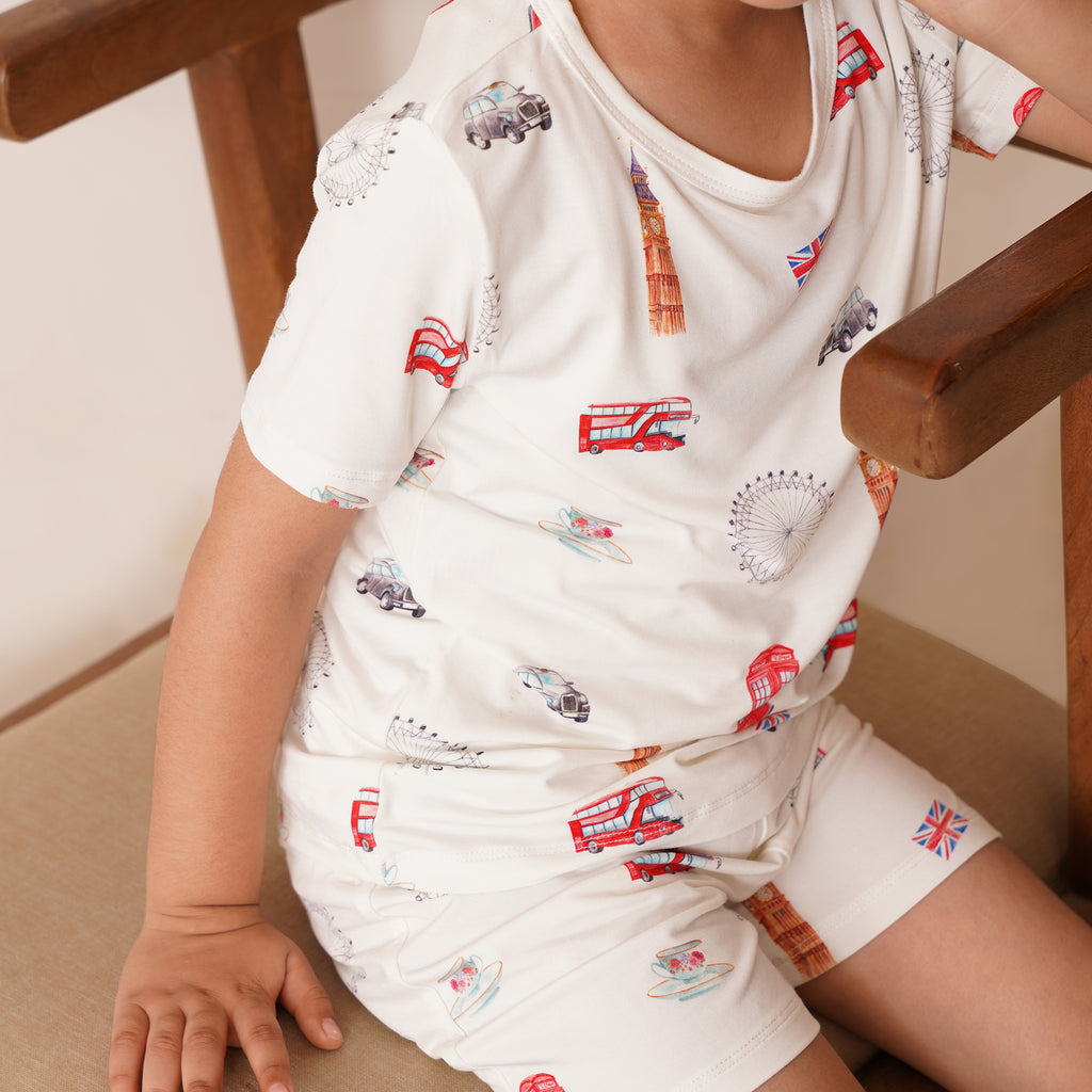 Child wearing a white outfit with london themed graphics sitting on a wooden chair.