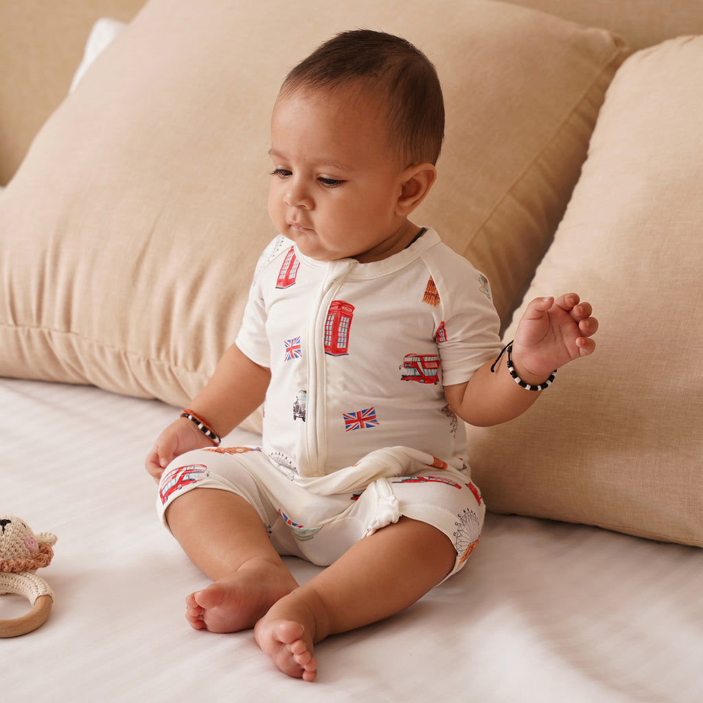 Baby sitting on a couch wearing a white outfit with red text and British flag designs.