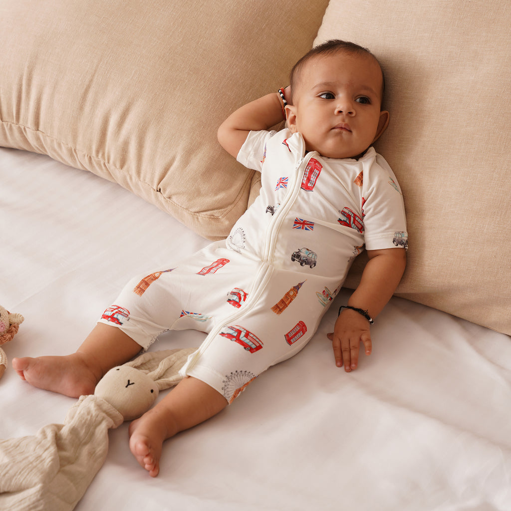 Baby wearing a white onesie with london themed designs, sitting on a beige couch.