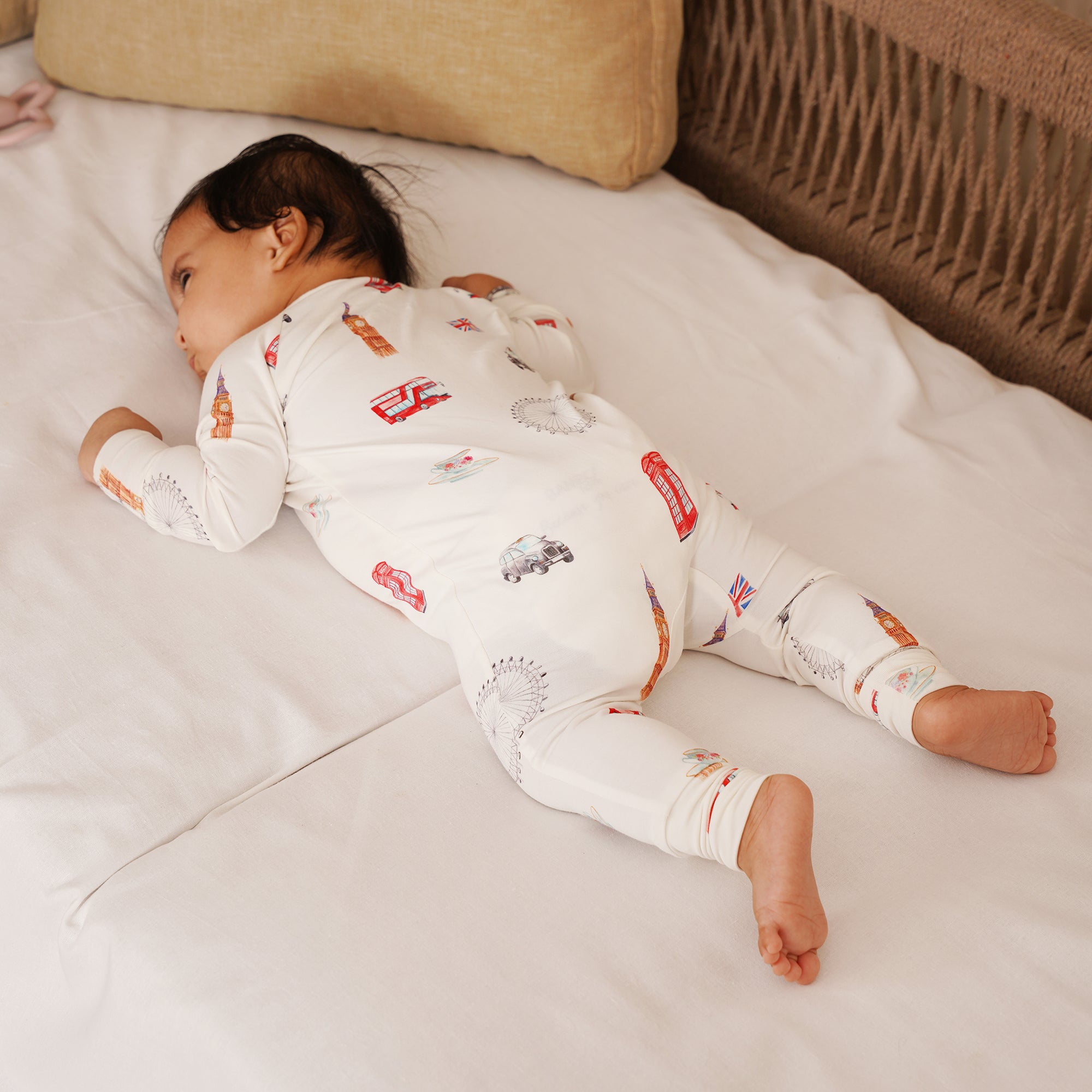 Baby lying on a couch wearing a white onesie with london pattern