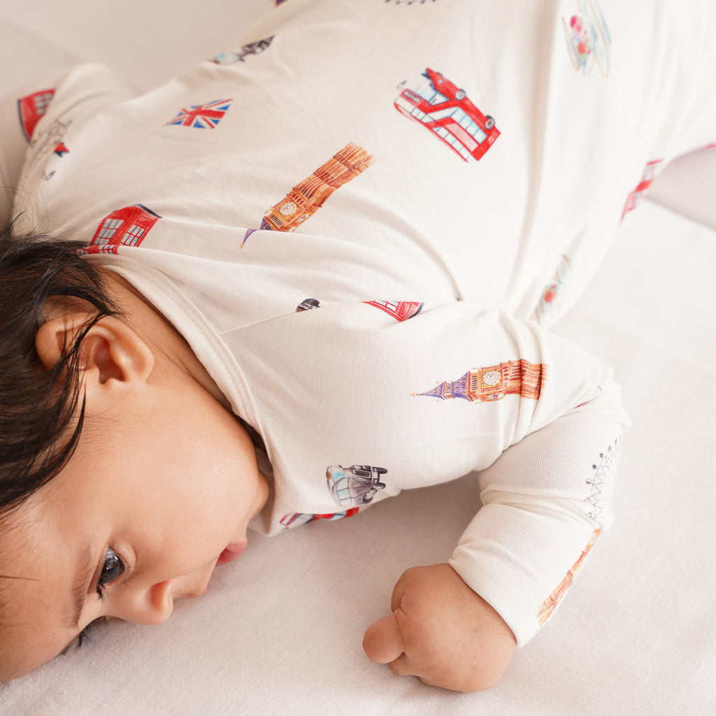 Baby wearing a onesie with London-themed illustrations, lying on a white surface.