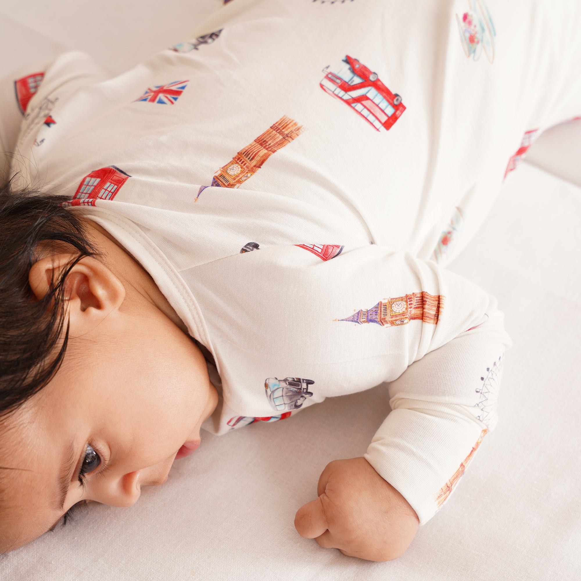 Baby wearing a onesie with London-themed illustrations, lying on a white surface.