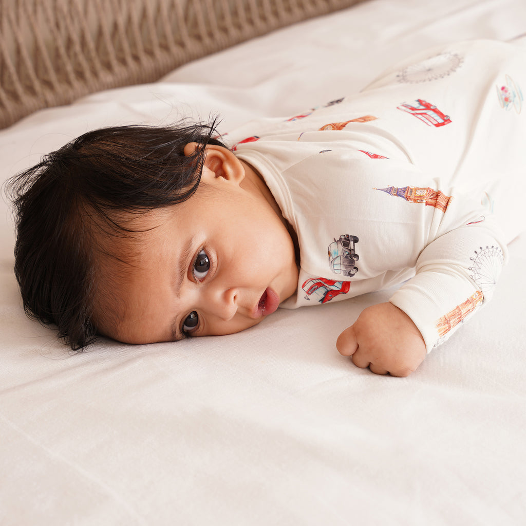 Baby lying on a white wearing a white onesie with london themed designs.