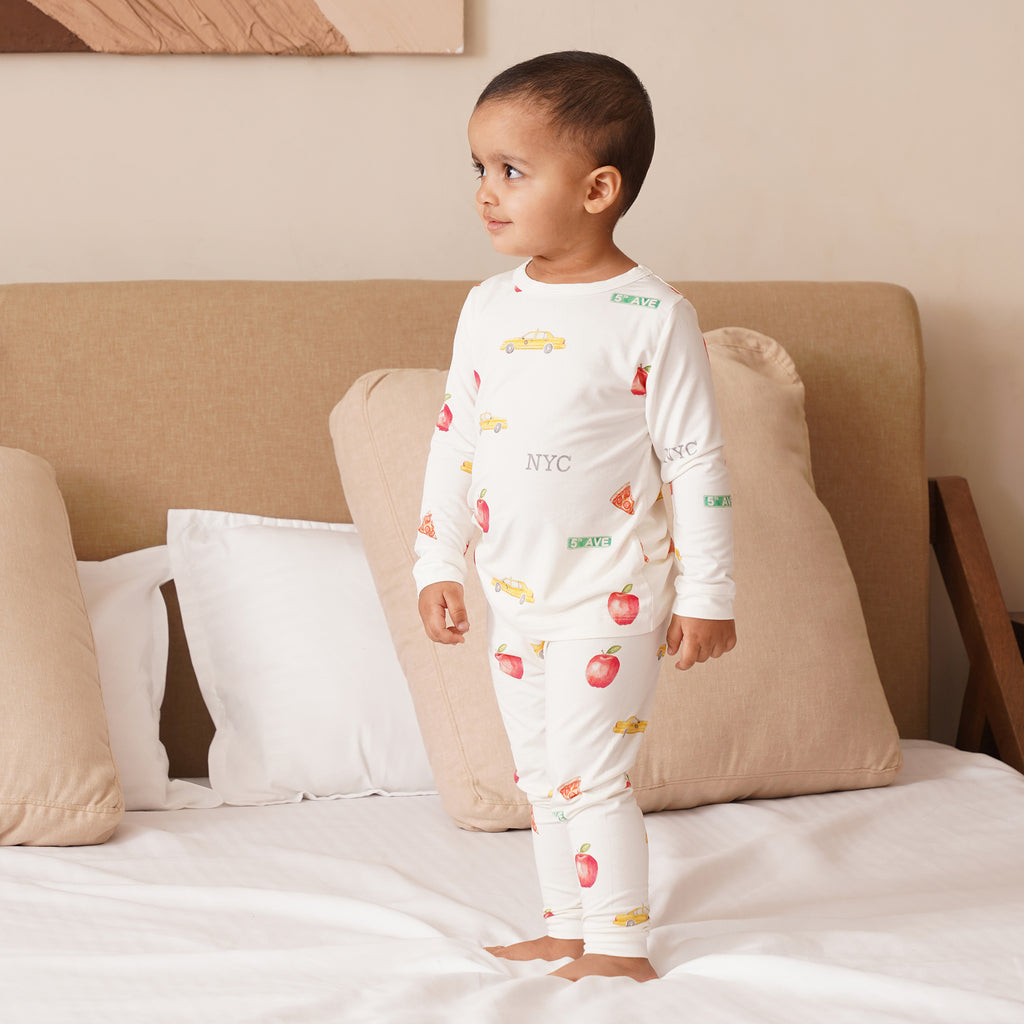 Child wearing a white pajama set with NYC patterns on a bed.