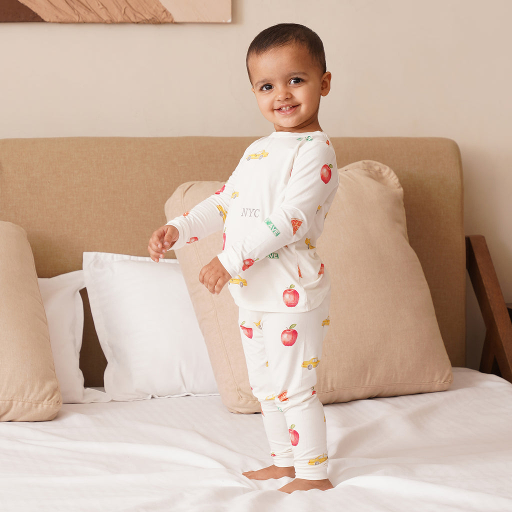 Child wearing a white outfit with NYC patterns on a bed