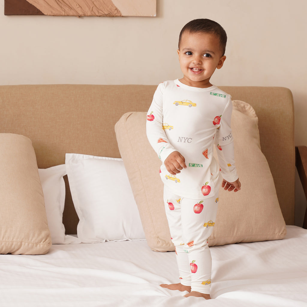 Child wearing a white long pajamas with colorful NYC themed patterns on a bed
