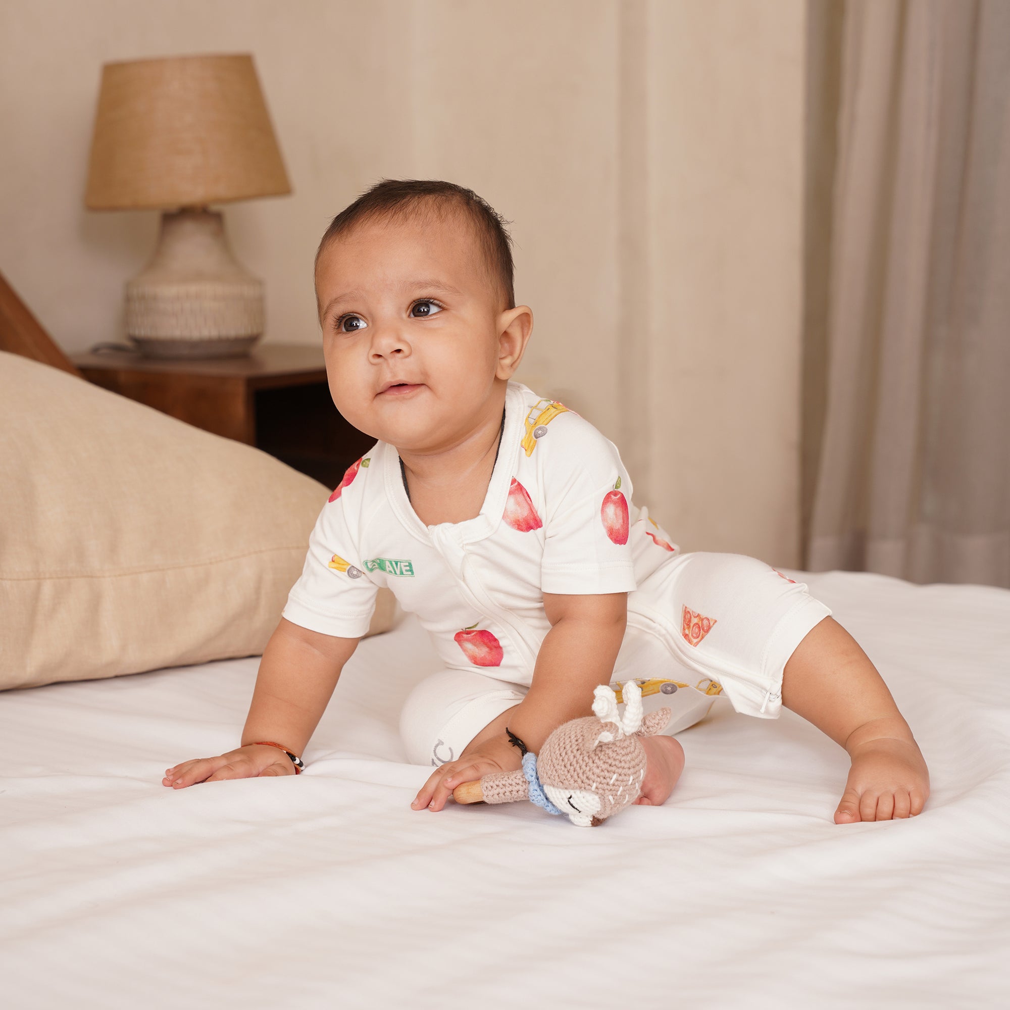 Baby in a white shortie outfit with NYC themed patterns on a bed