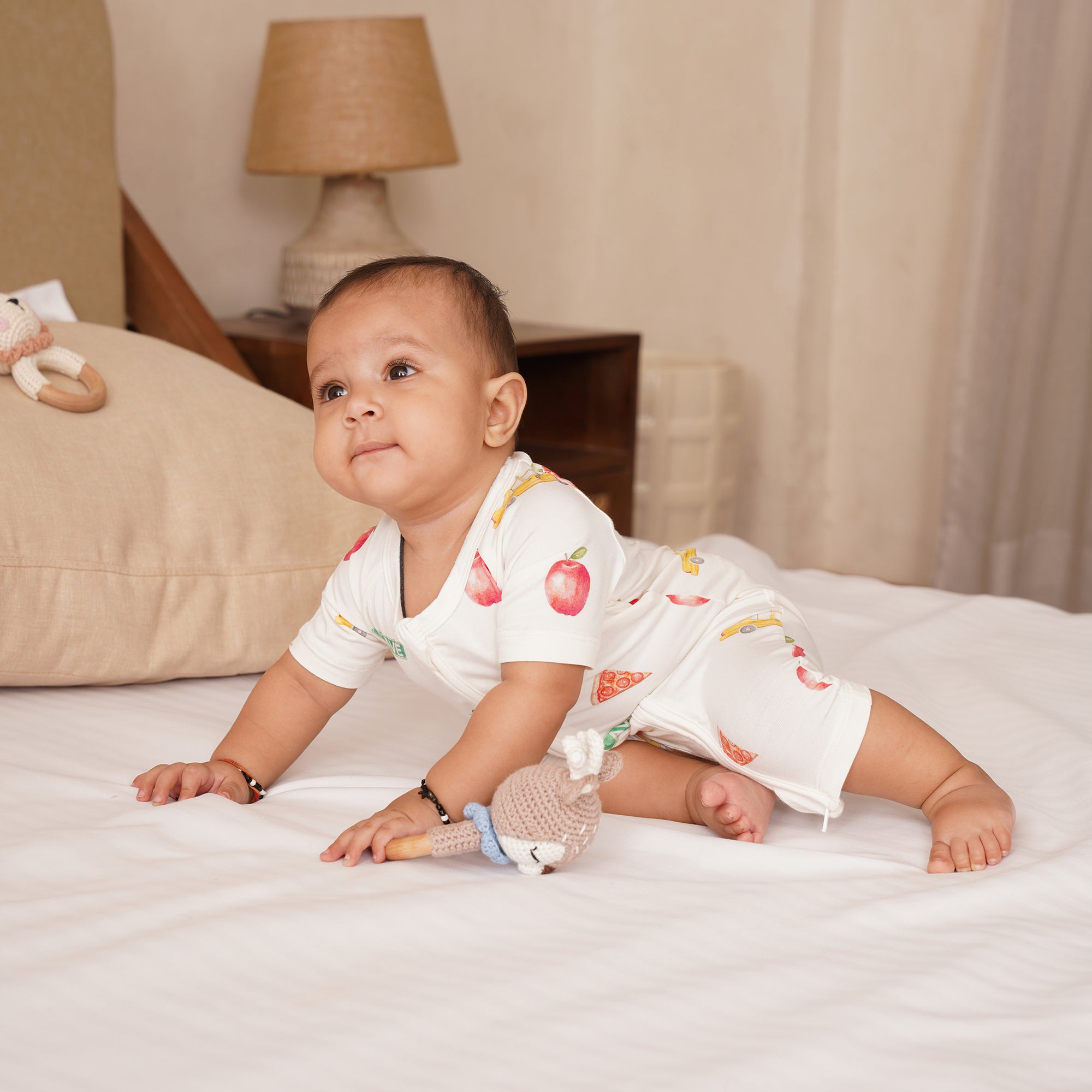Baby in a white outfit with NYC patterns on a bed