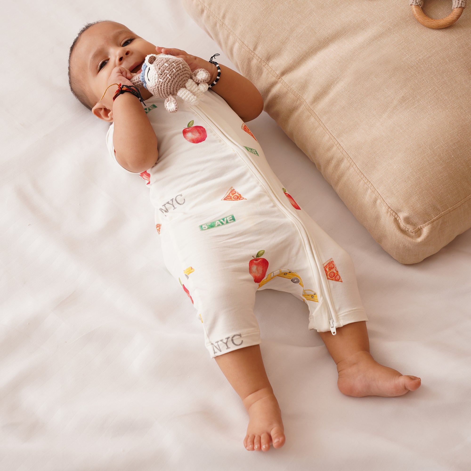 Baby lying on a white surface with a beige pillow and wooden toy in the background in NYC themed outfit