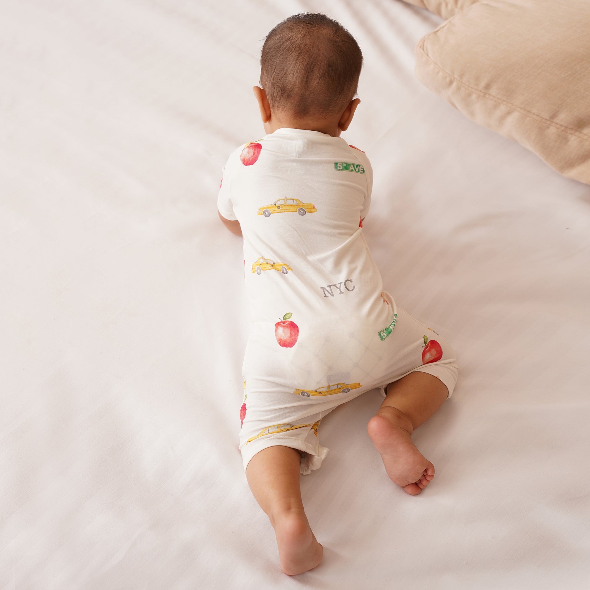 Baby wearing a white shortie with colorful NYC prints on a light-colored surface