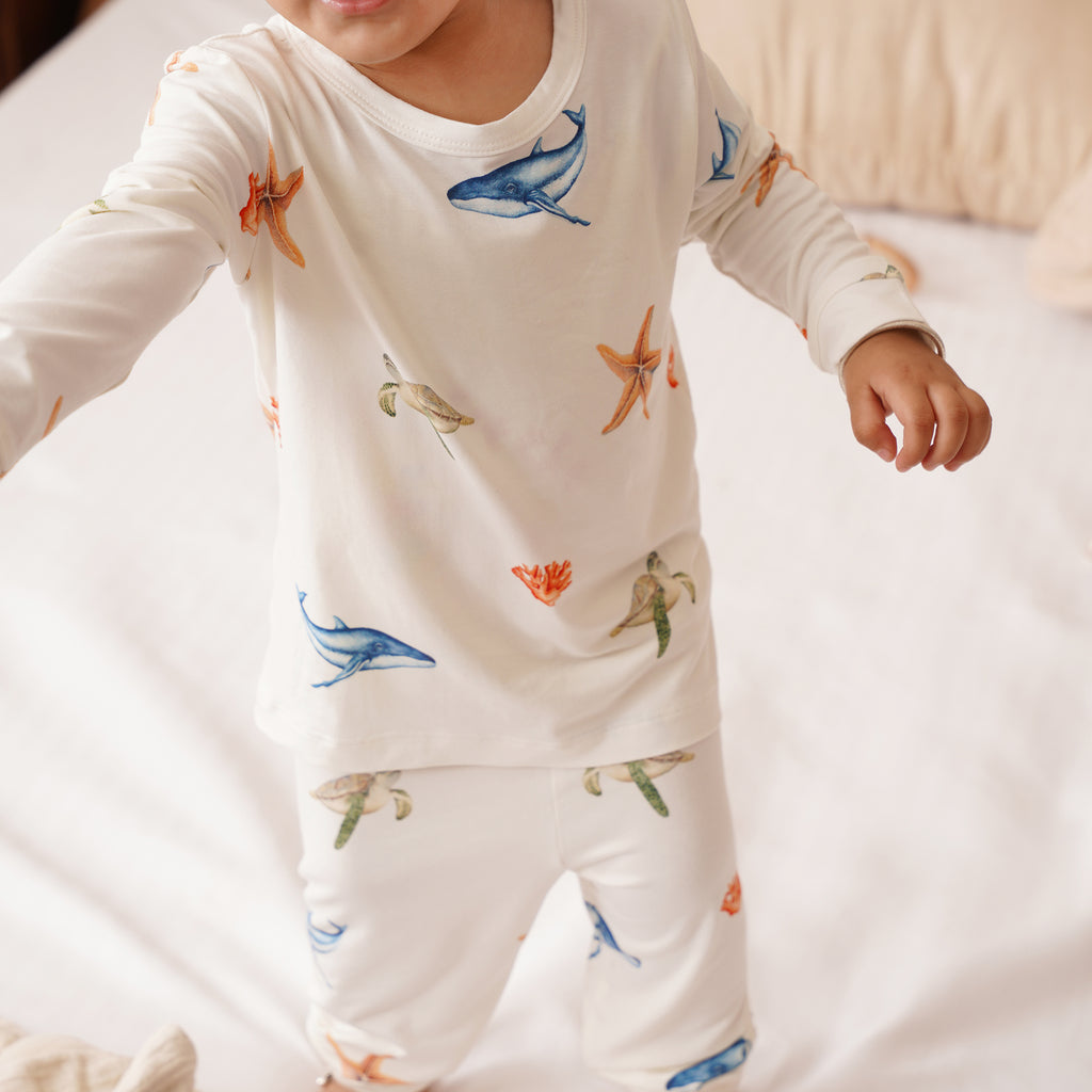 Child wearing a white long-sleeve shirt and pants with colorful under the sea prints on a light background.