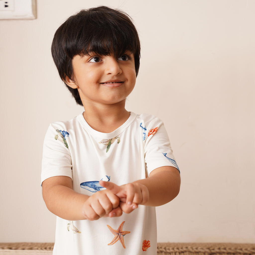 Child wearing a white shirt with colorful under the sea designs on a plain background