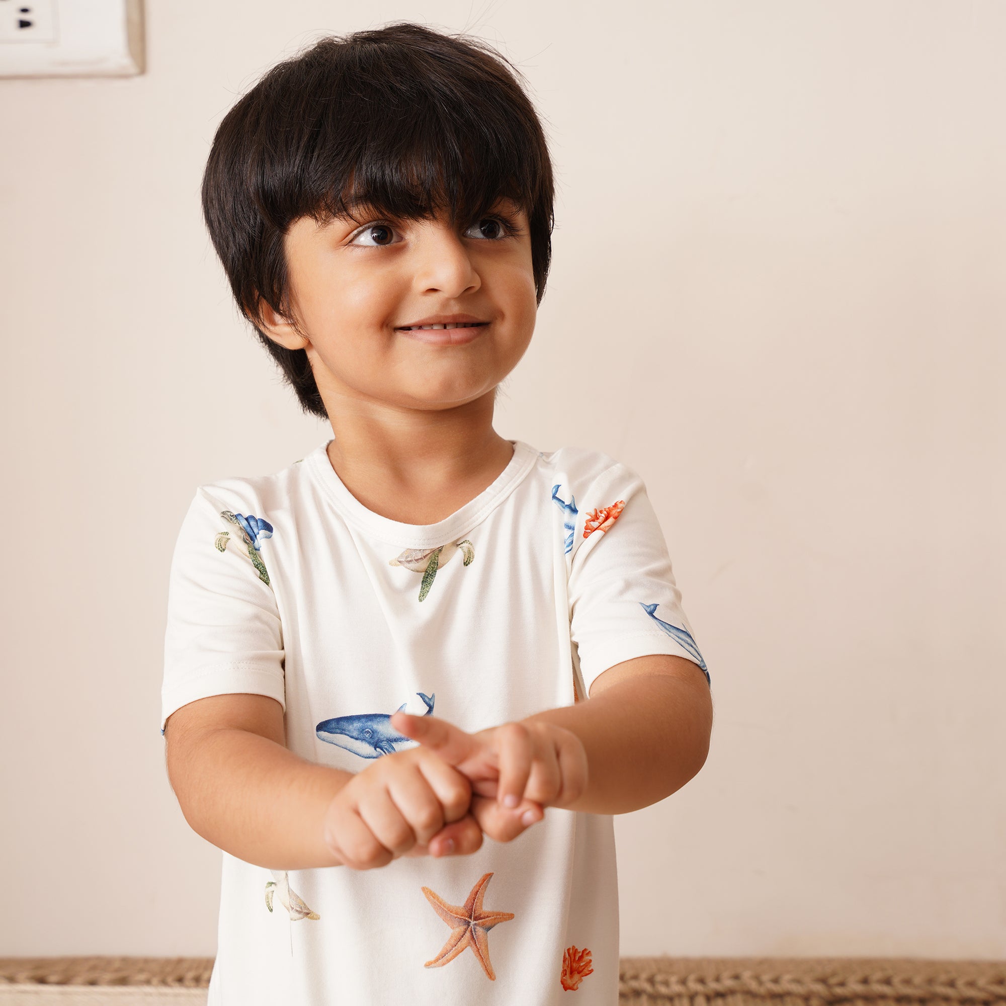 Child wearing a white shirt with colorful under the sea designs on a plain background