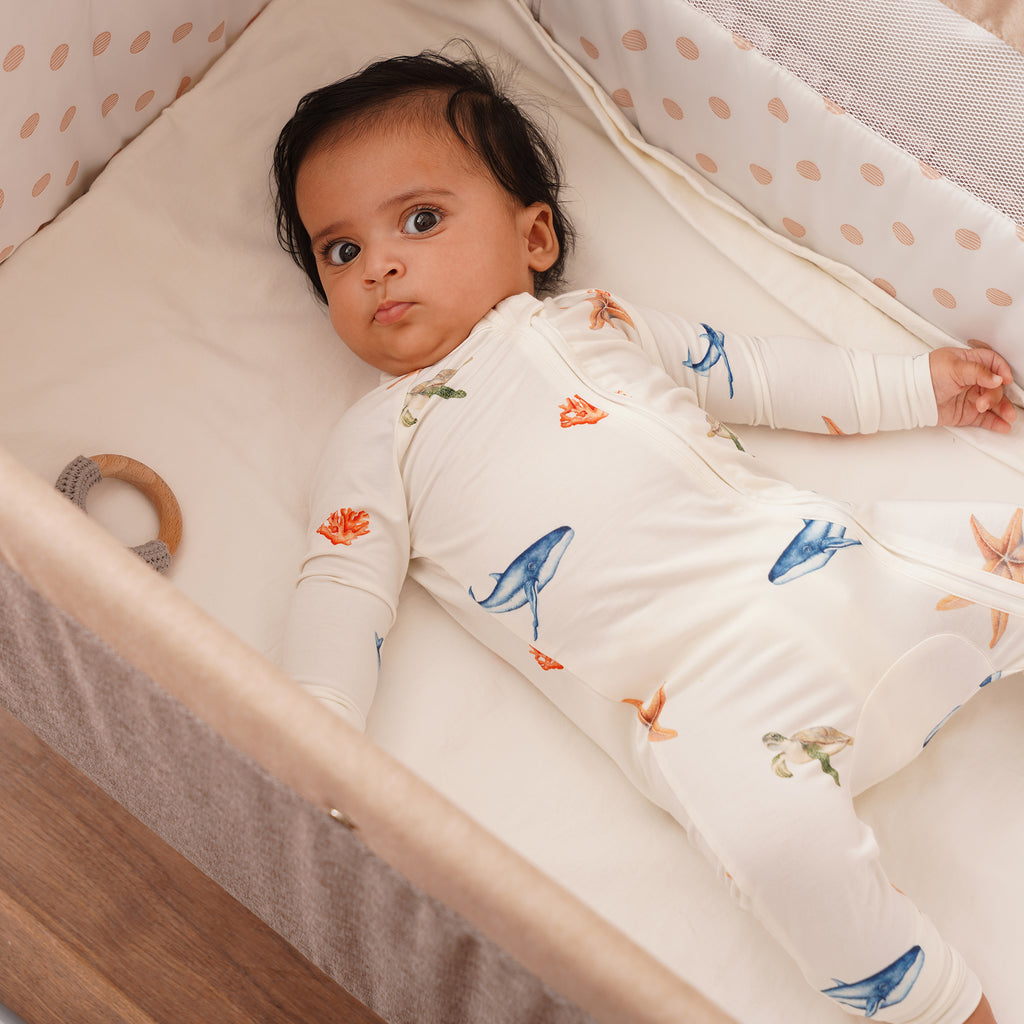 Baby lying in a crib wearing a onesie with whale patterns.