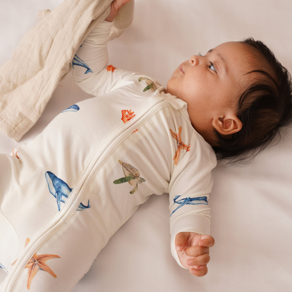 Baby wearing a cream-colored outfit with colorful sea creature patterns on a white surface